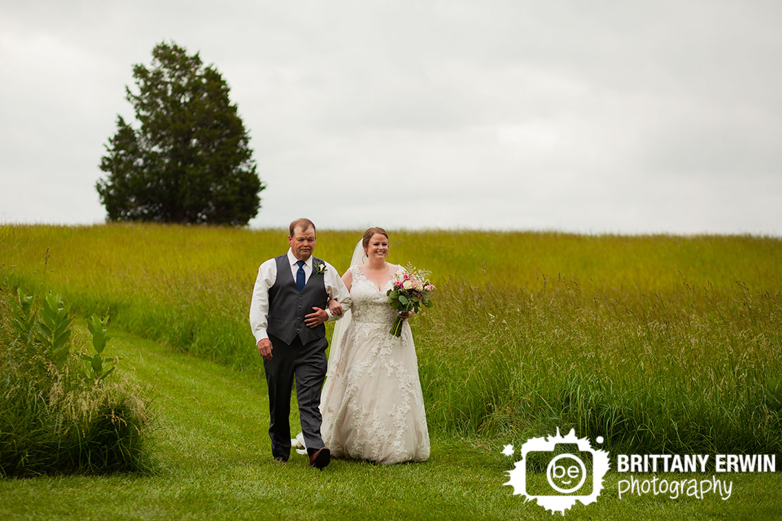 bride-walking-down-aisle-with-father-tall-grass-outdoor-ceremony.jpg