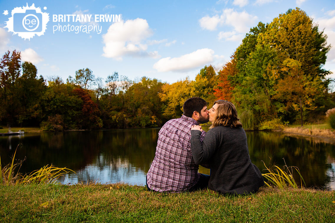 Fall-foliage-autumn-leaves-couple-sit-on-hill-by-pond-at-sunset.jpg