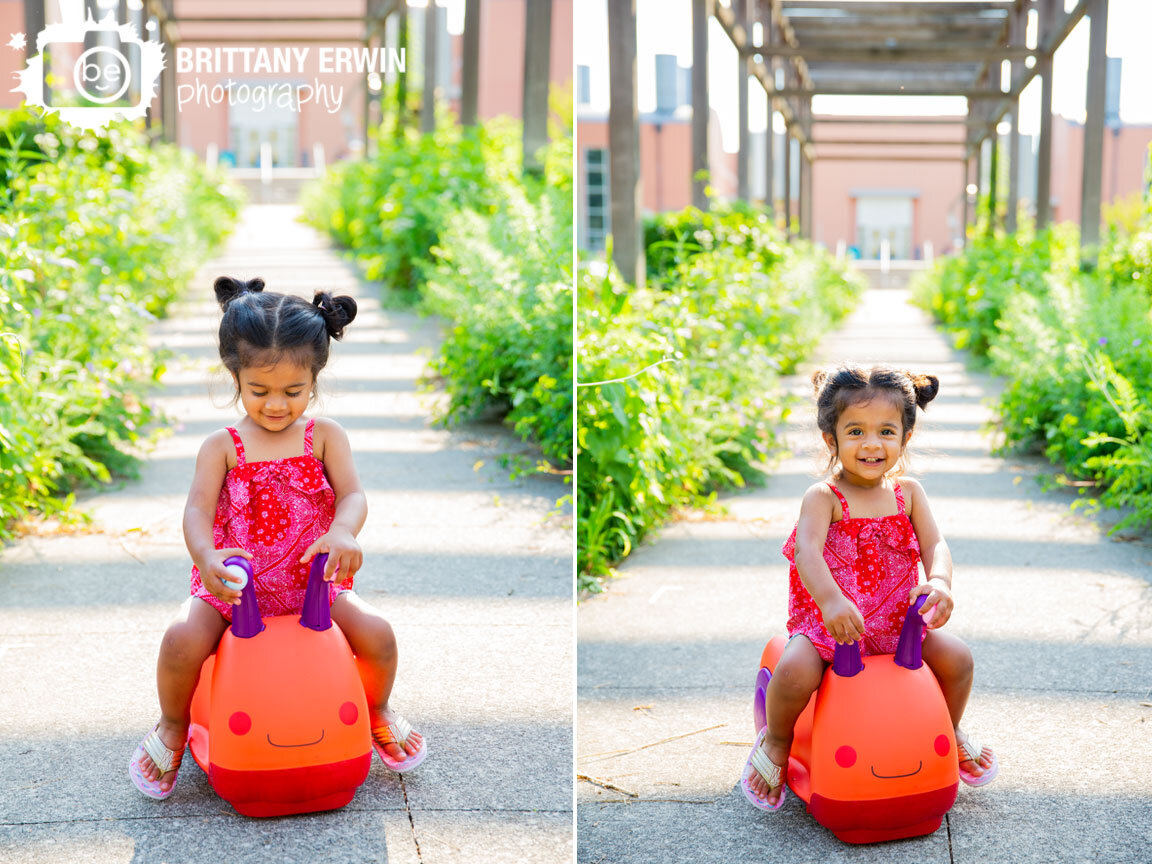 Indianapolis-Art-Center-portrait-photographer-toddler-girl-riding-on-toy-slug-car-outdoor.jpg