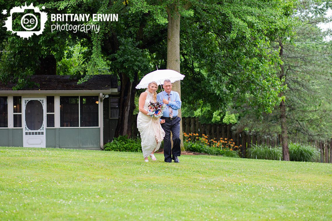 Outdoor-rainy-day-wedding-photographer-white-umbrella-bride-with-father-walking-down-aisle.jpg