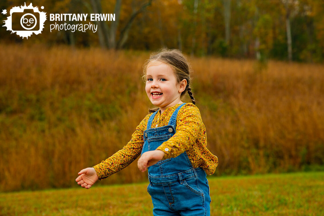 little-girl-playing-outside-fall-tall-grasses-yellow-shirt-overalls.jpg