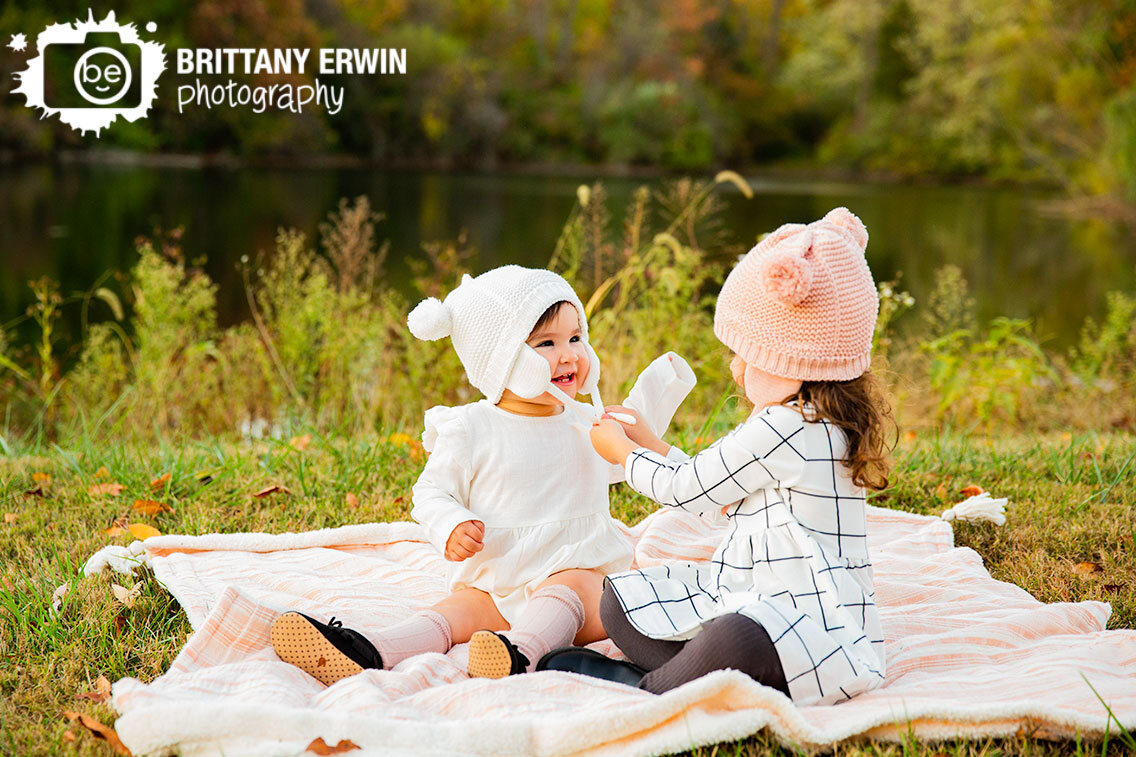 Indianapolis-fall-family-portrait-photographer-sisters-play-on-blanket-by-pond.jpg