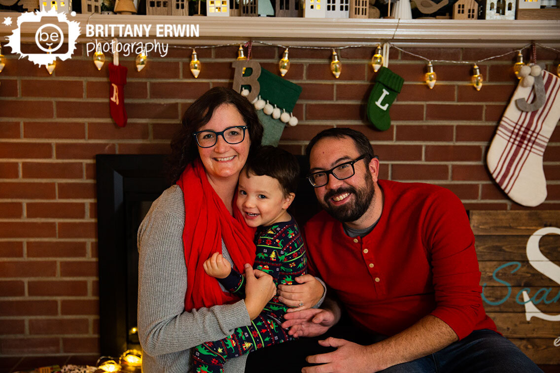Indianapolis-family-portrait-photographer-parents-with-son-sitting-in-front-of-fireplace-with-stockings.jpg