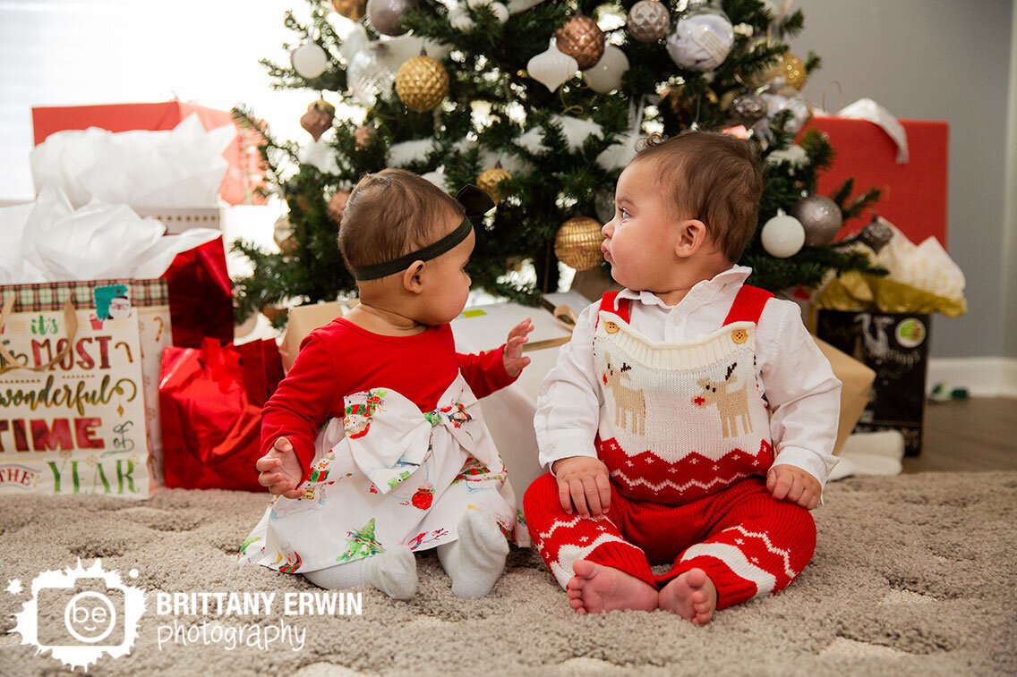 Twins-with-Christmas-tree-gifts-looking-at-each-other-in-home-session.jpg