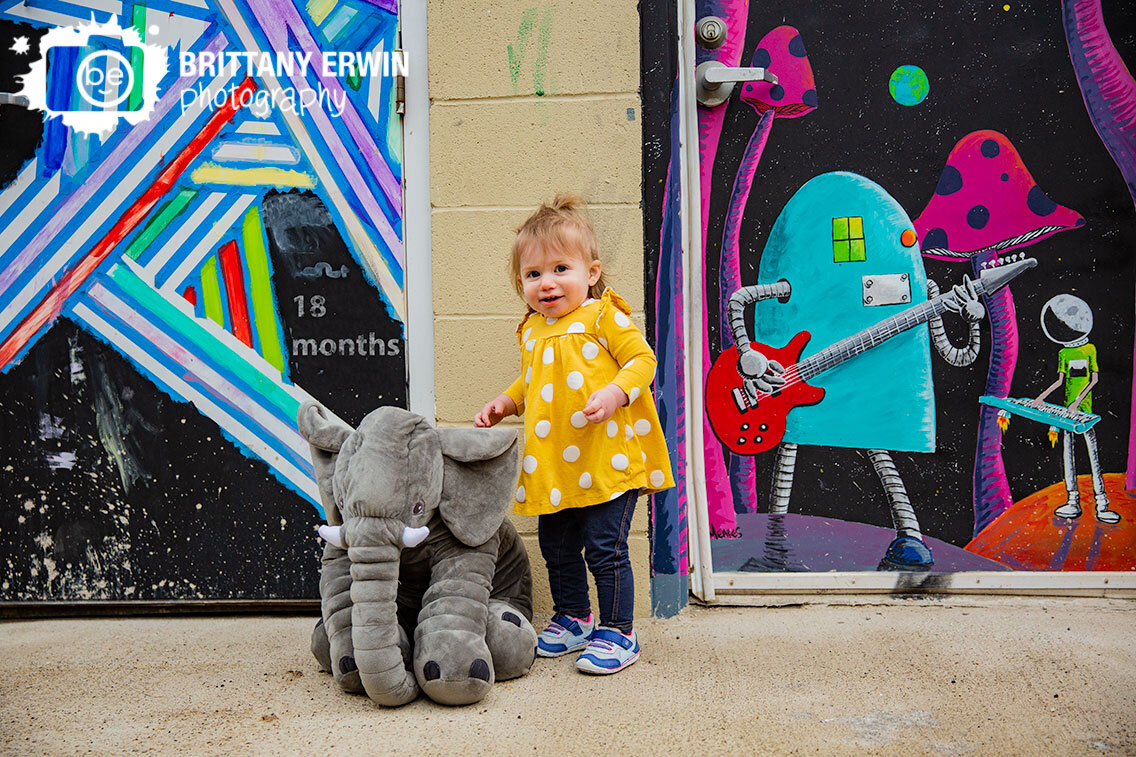 Fountain-Square-Indiana-milestone-portrait-photographer-stuffed-elephant-toddler-girl-mural.jpg