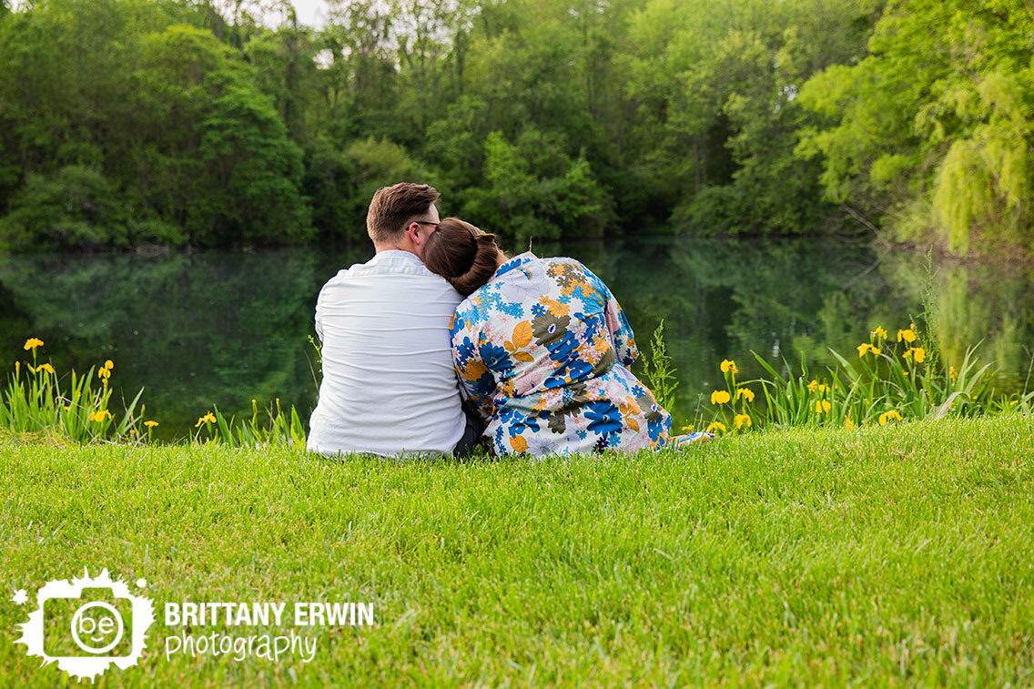 couple-sitting-by-pond-with-yellow-irises-tree-lined-water.jpg