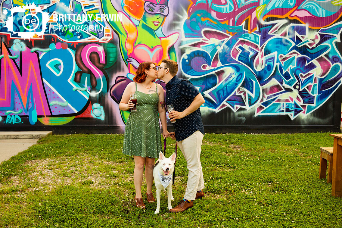 Rad-brewery-engagement-portrait-couple-outside-with-retro-mural-with-pet-dog.jpg