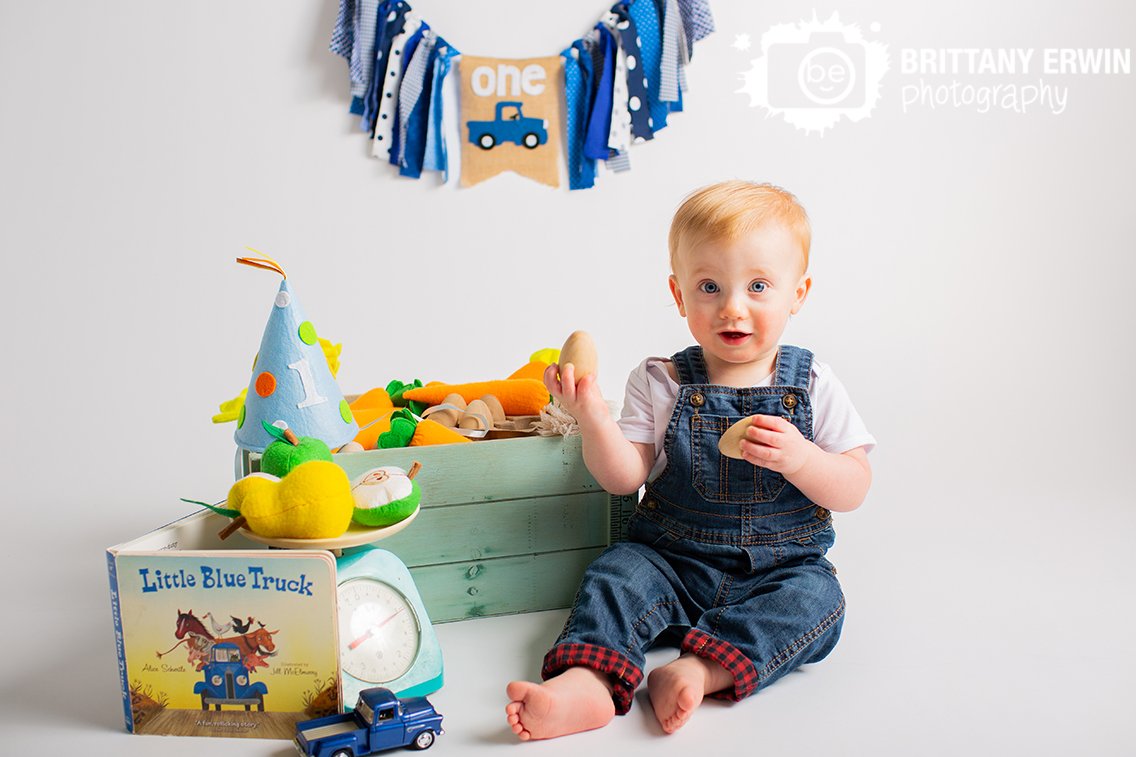 baby-boy-first-birthday-photographer-playing-with-wooden-eggs-little-blue-truck-theme-book-crate-of-veggies.jpg