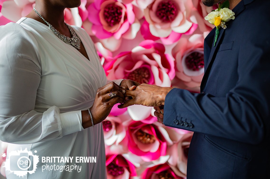 Indianapolis-elopement-photographer-couple-exchange-rings-with-pink-flower-background.jpg