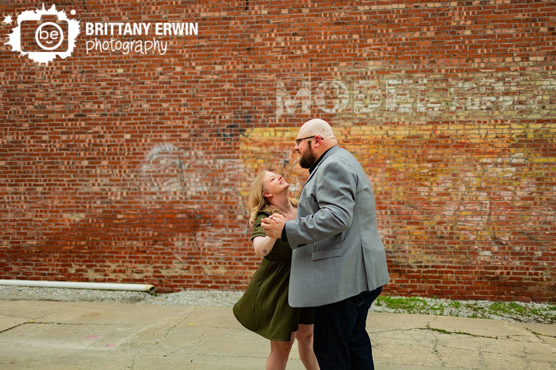 Fountain-Square-engagement-portrait-photographer-couple-dancing-by-brick-wall.jpg