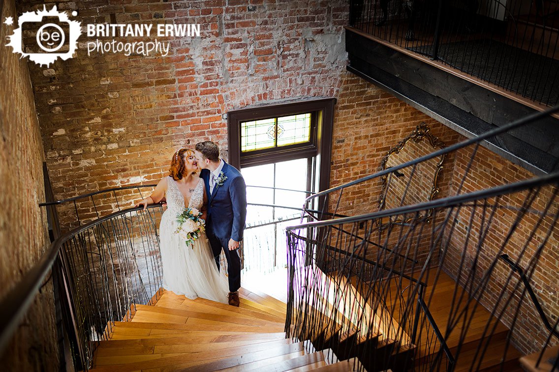 Indianapolis-St-joseph-hall-wedding-photographer-couple-walking-up-spiral-grand-staircase-with-custom-iron-railing-in-sunbeam.jpg