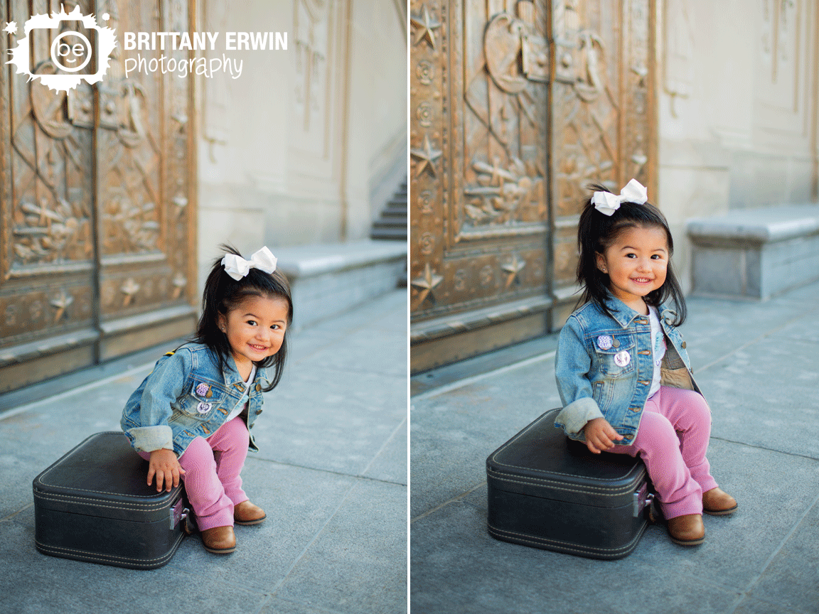 Indianapolis-portrait-photographer-first-birthday-girl-sitting-on-antique-suitcase-with-gold-doors.gif
