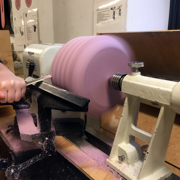 Carly makes good use of the lathe in shaping this cylindrical form, and John says, "This stuff cuts like butter'‘.