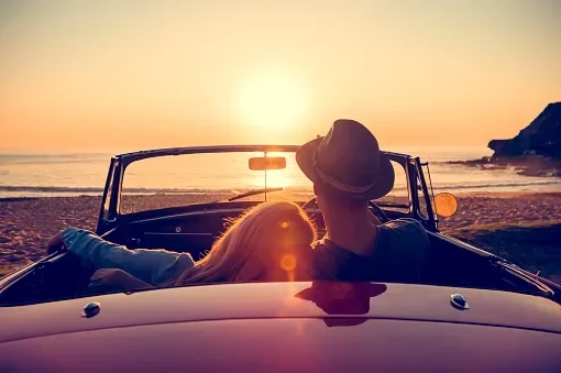 Couple sitting in a convertible car watching the sunset on the beach