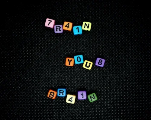 Colorful alphabet beads spelling out "TRAIN," "YOU," and "BRAND" on a black textured surface.