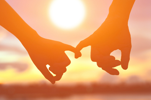 Two hands forming a heart shape with the sunset in the background.