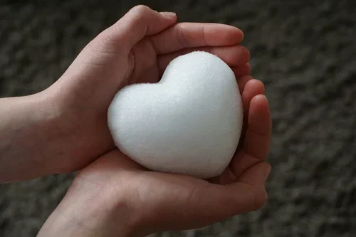 Two hands holding a white heart-shaped object made of foam or a similar material.
