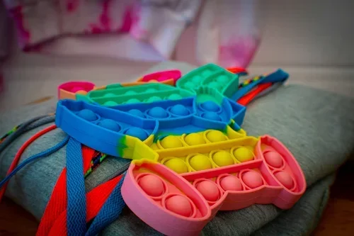 Colorful silicone lacing toys with loops in pink, yellow, green, blue, and red, placed on a gray surface.