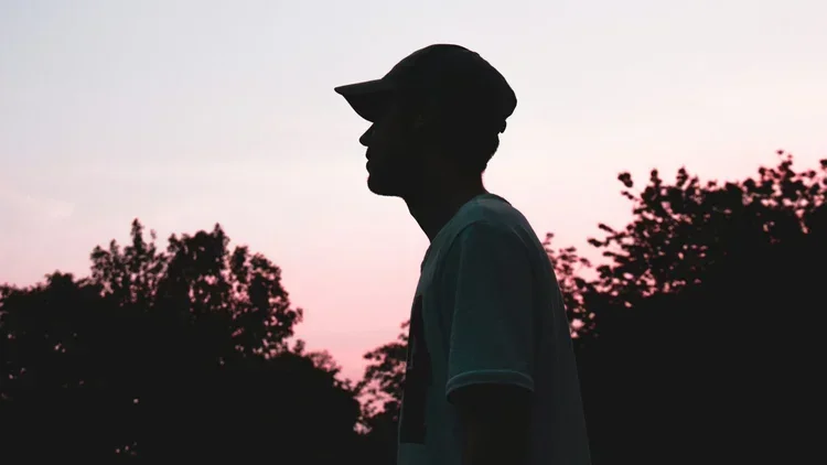 Silhouette of a person wearing a cap at sunset with trees in the background.