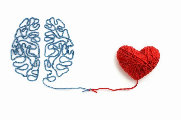 A blue string in the shape of a human brain connects to a red heart-shaped ball of yarn with thread.