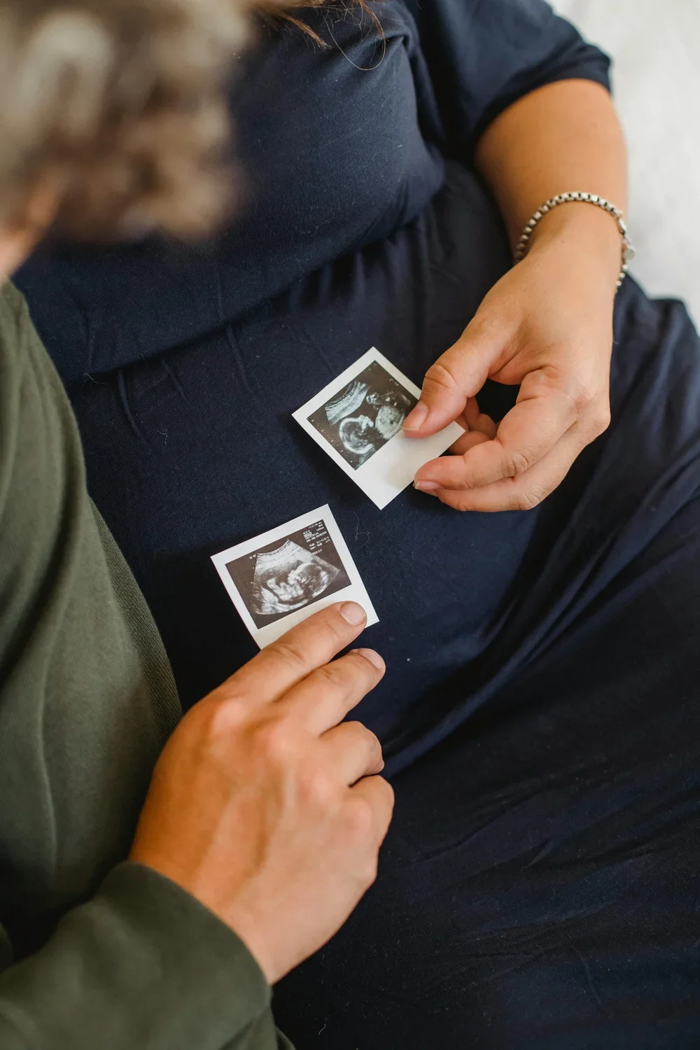 Person holding two ultrasound scan pictures on lap.