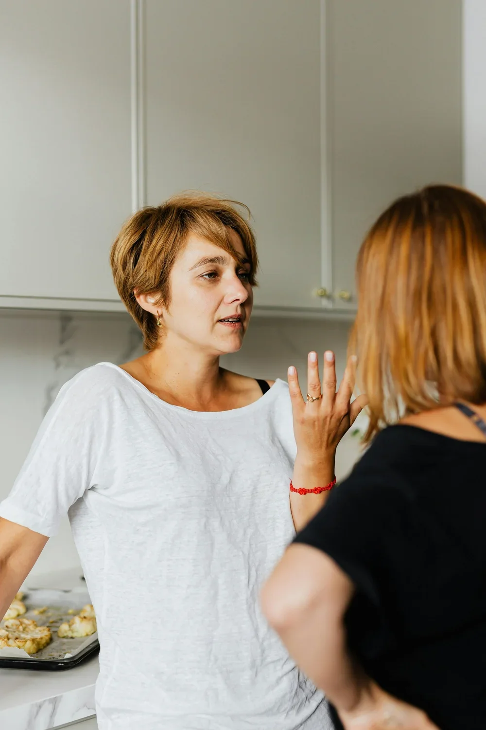 Two women are having a heated discussion in a kitchen, with one woman gesturing expressively as she speaks.