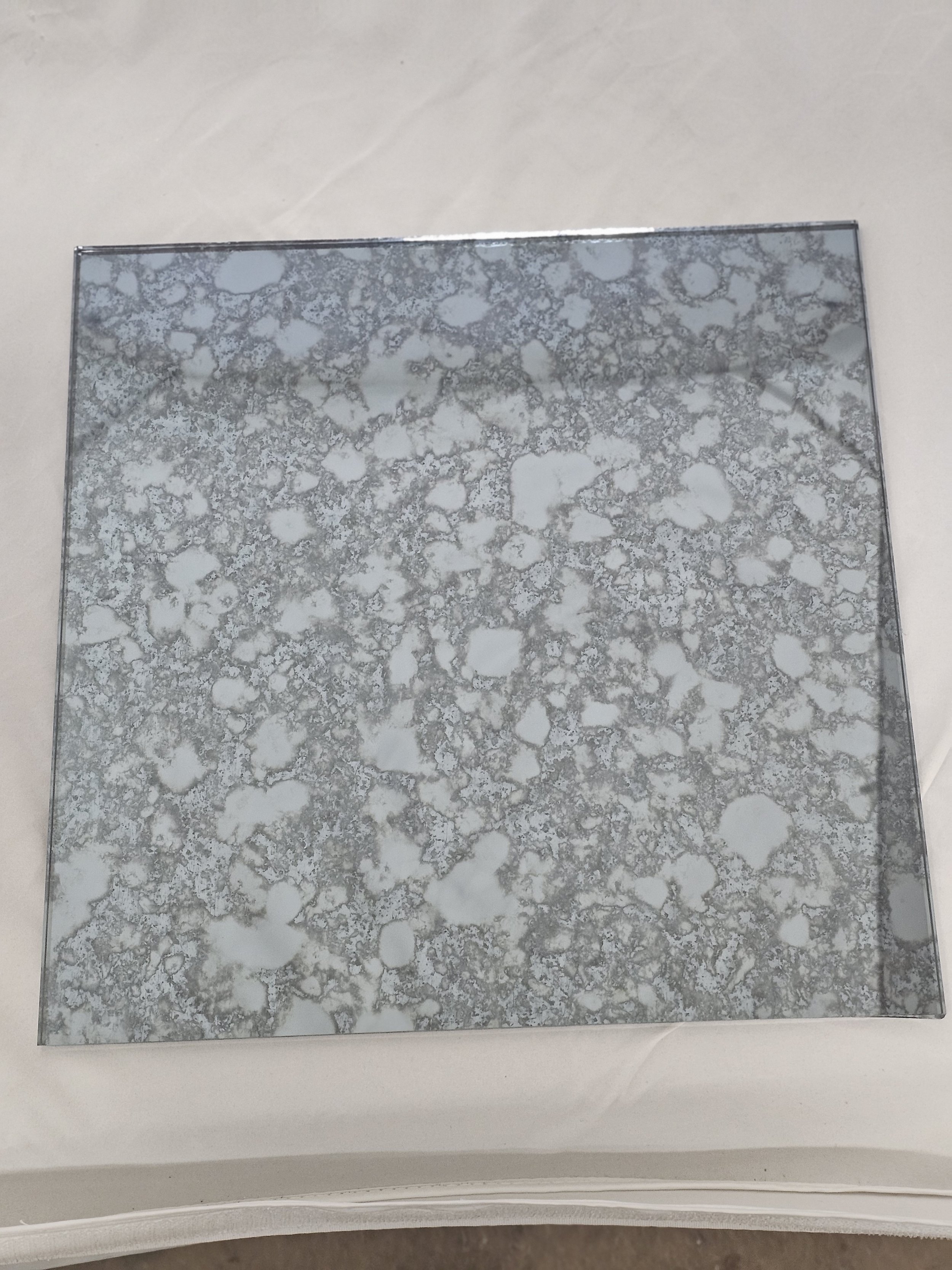A square reflective surface with a cloudy, speckled pattern, placed on a white background.