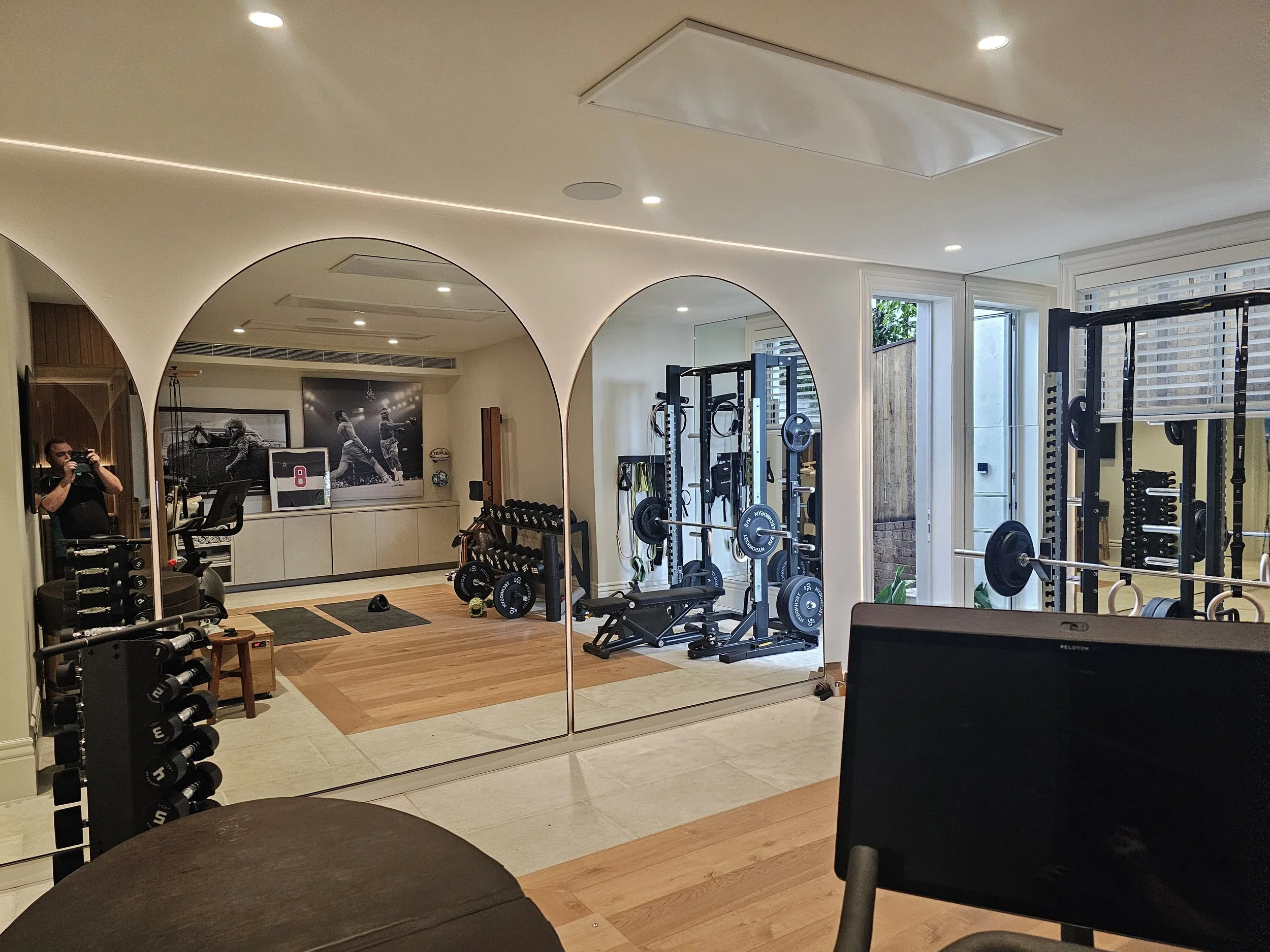 Home gym with exercise equipment including weights, a rowing machine, and a mirror, decorated with sports posters.