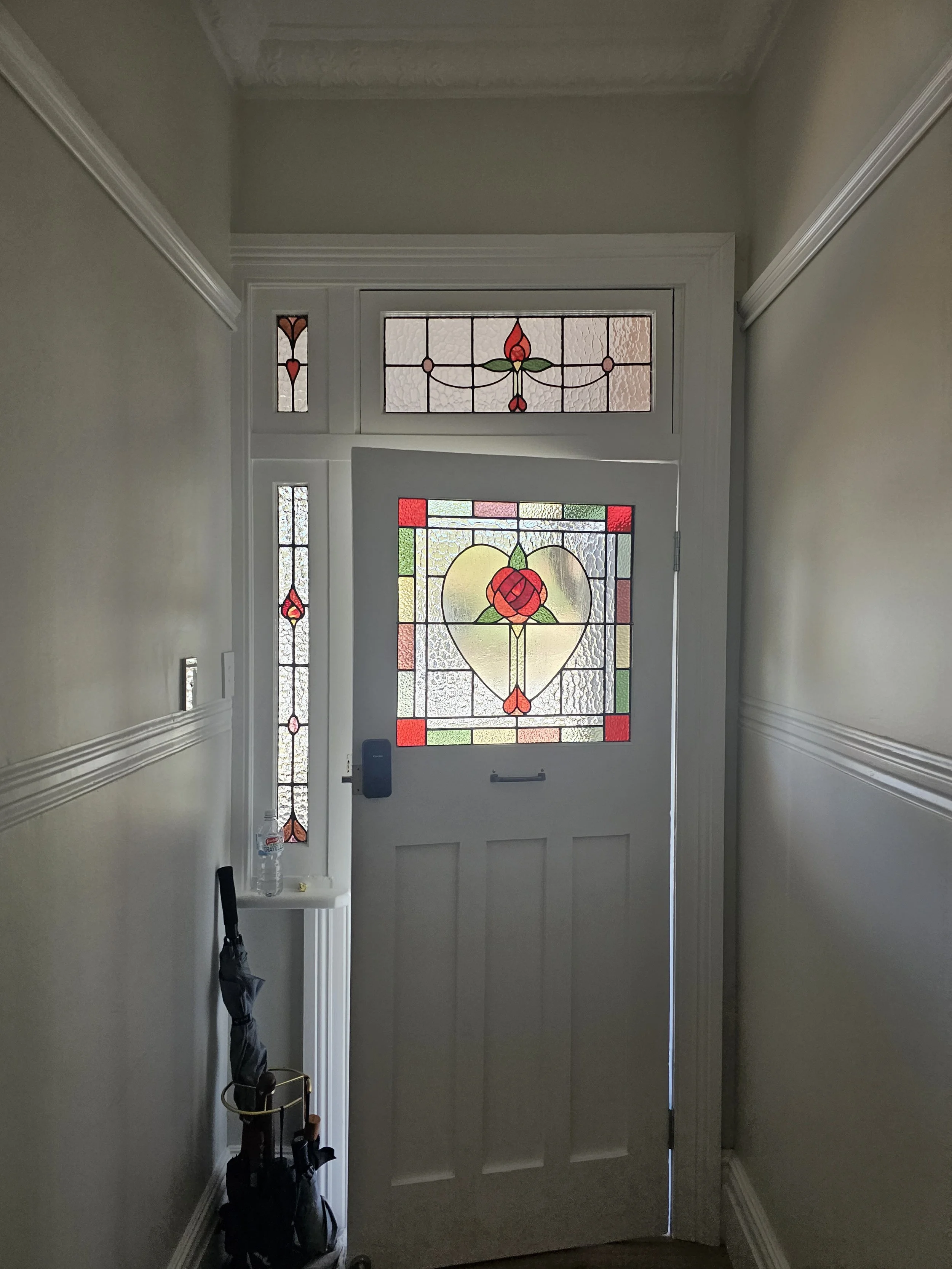 Front door with stained glass window panels featuring floral and heart motifs, located in a hallway with beige walls and white trim.