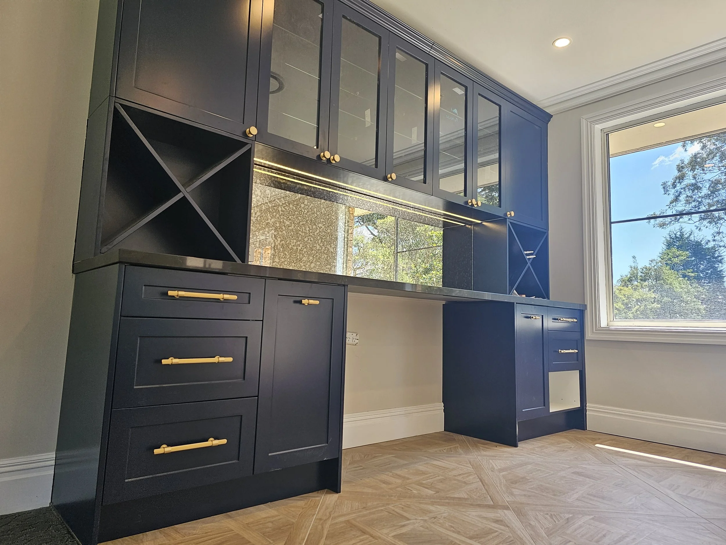 Blue kitchen cabinets with gold handles and a large window with a view of trees.