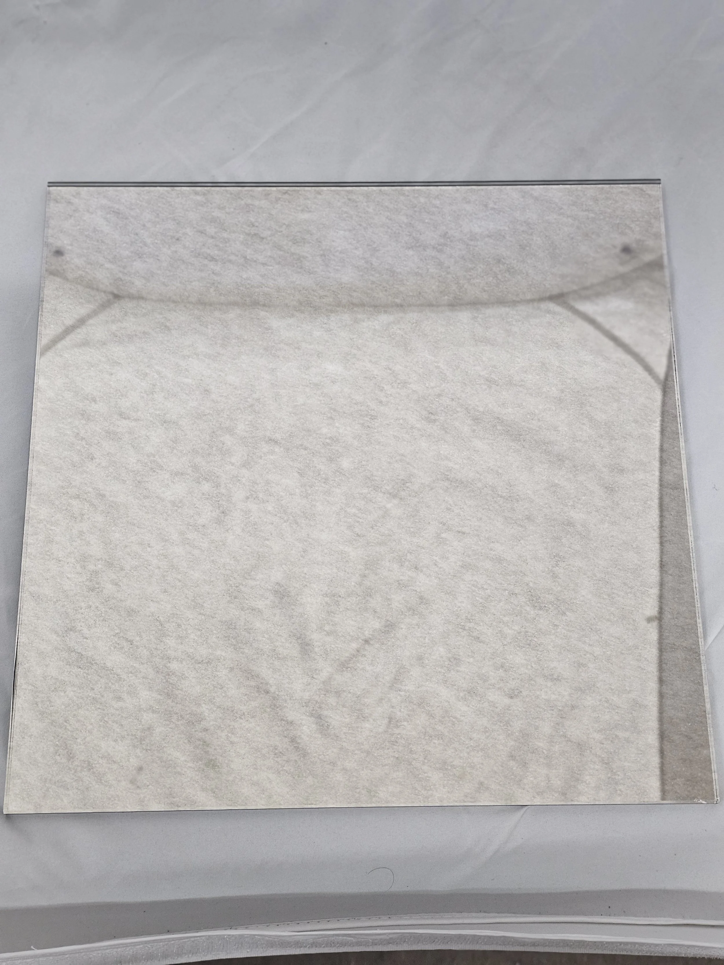 A square mirror with a paper backing, placed on a light-colored surface.