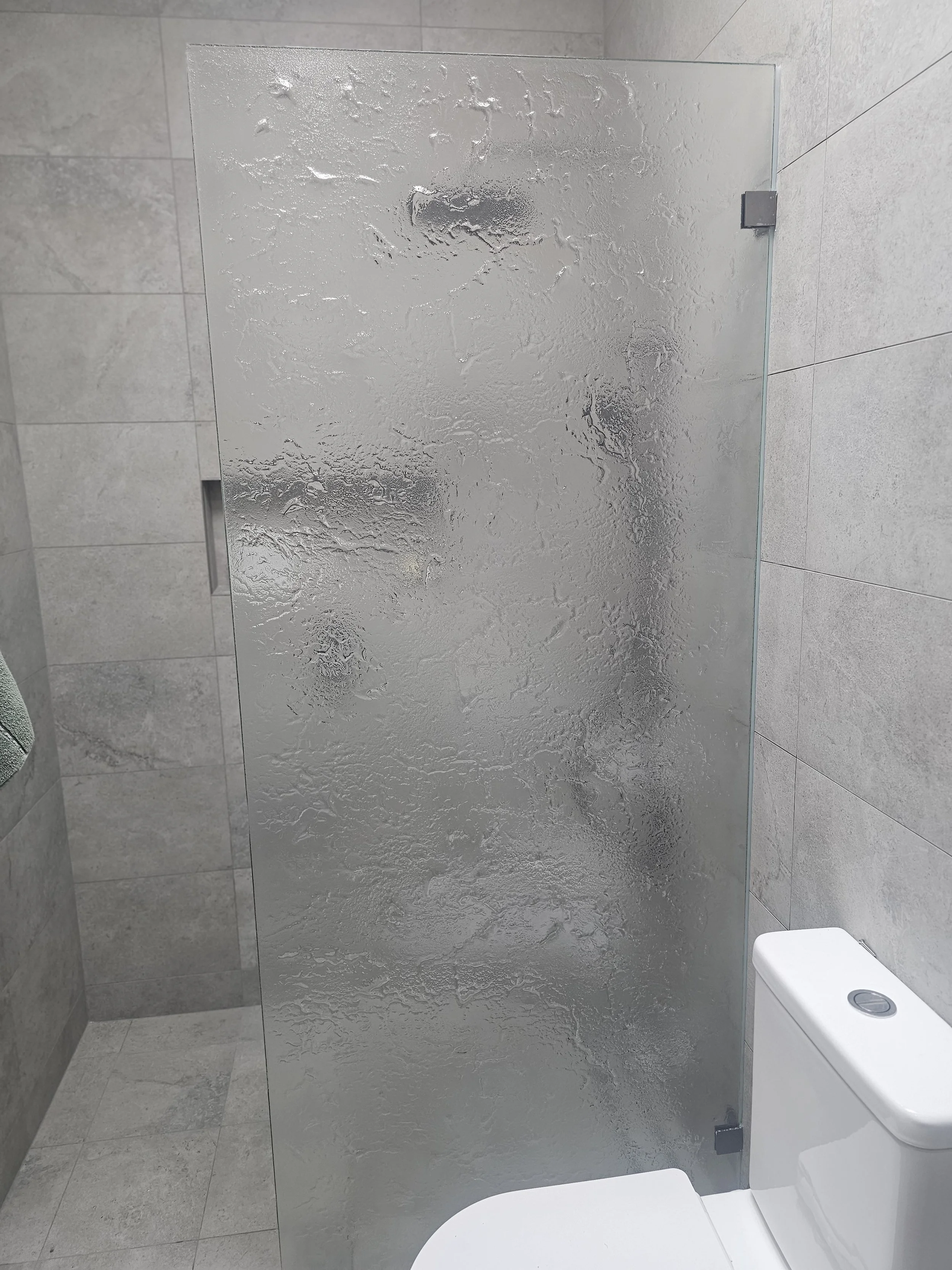 A bathroom with a frosted glass shower door, gray tiled walls, and a white toilet.