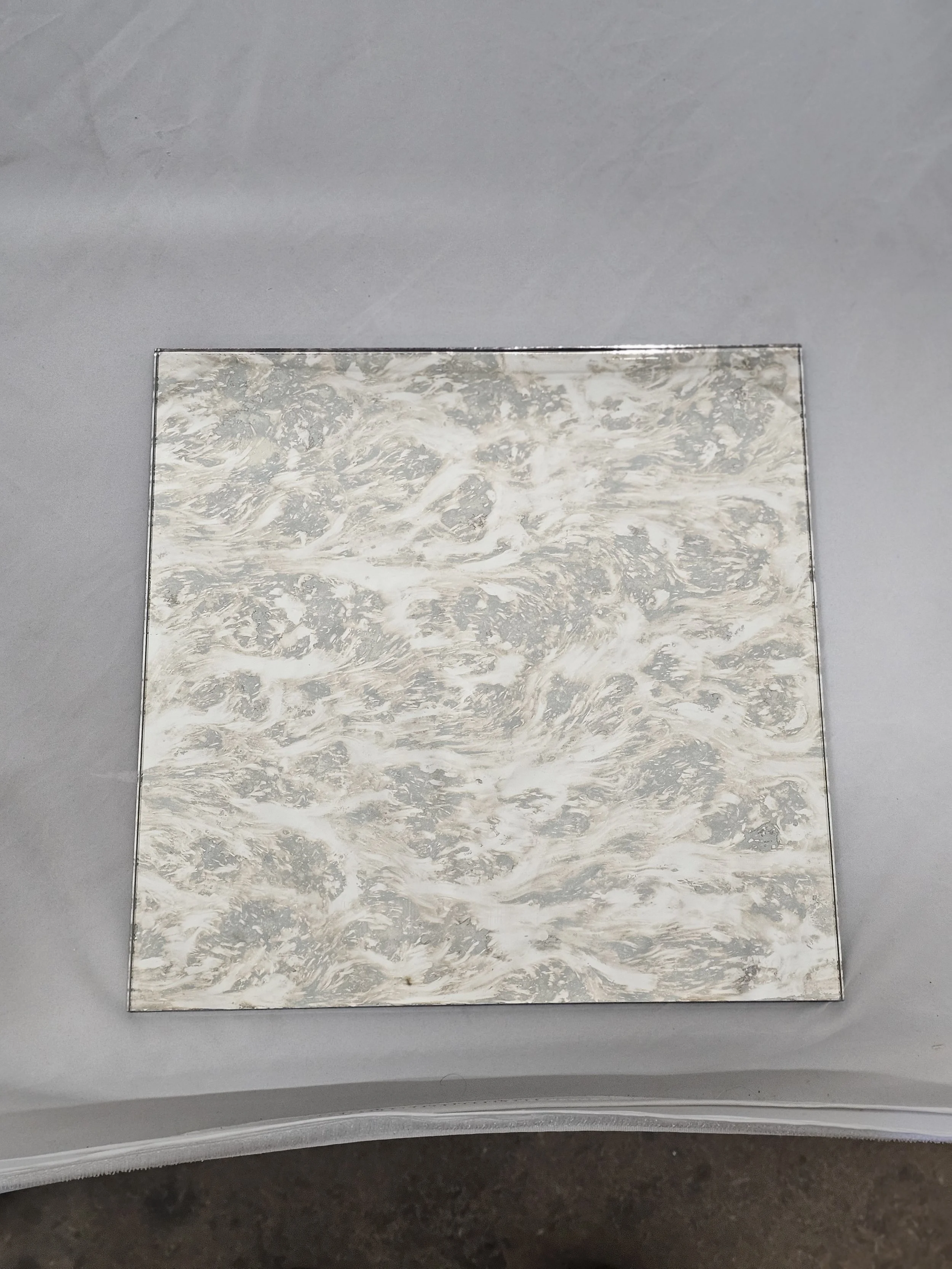 A square piece of material with a marbled pattern in beige and gray colors placed on a light gray surface.