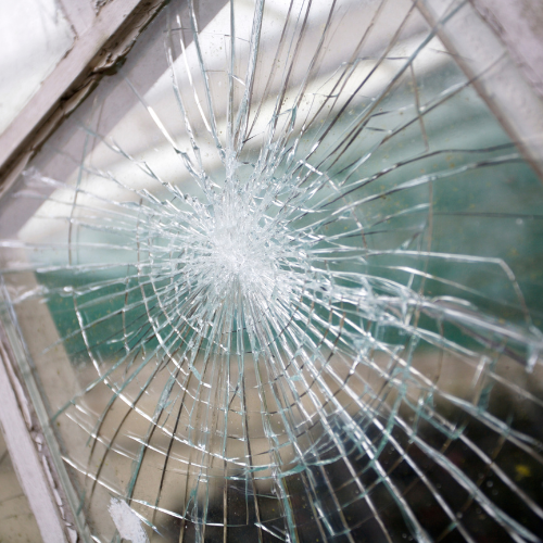 Close-up of a broken glass window with a spiderweb crack pattern.