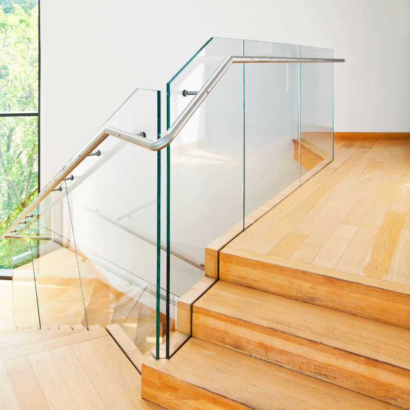 Interior view of a modern staircase with wooden steps, glass panels, and a metal handrail.