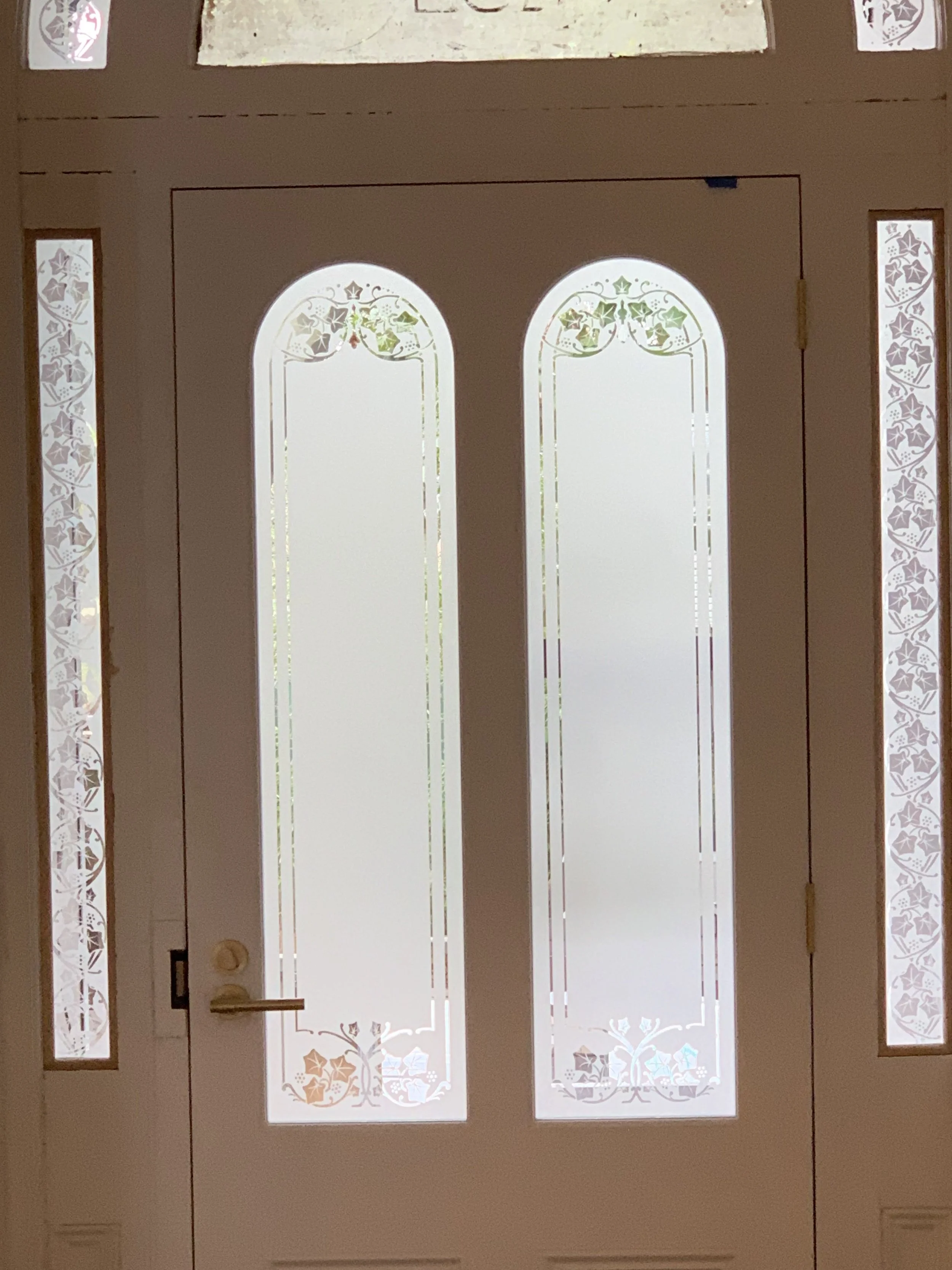 A white front door with Victorian-style glass panels and decorative etching, flanked by sidelights with matching etched designs.