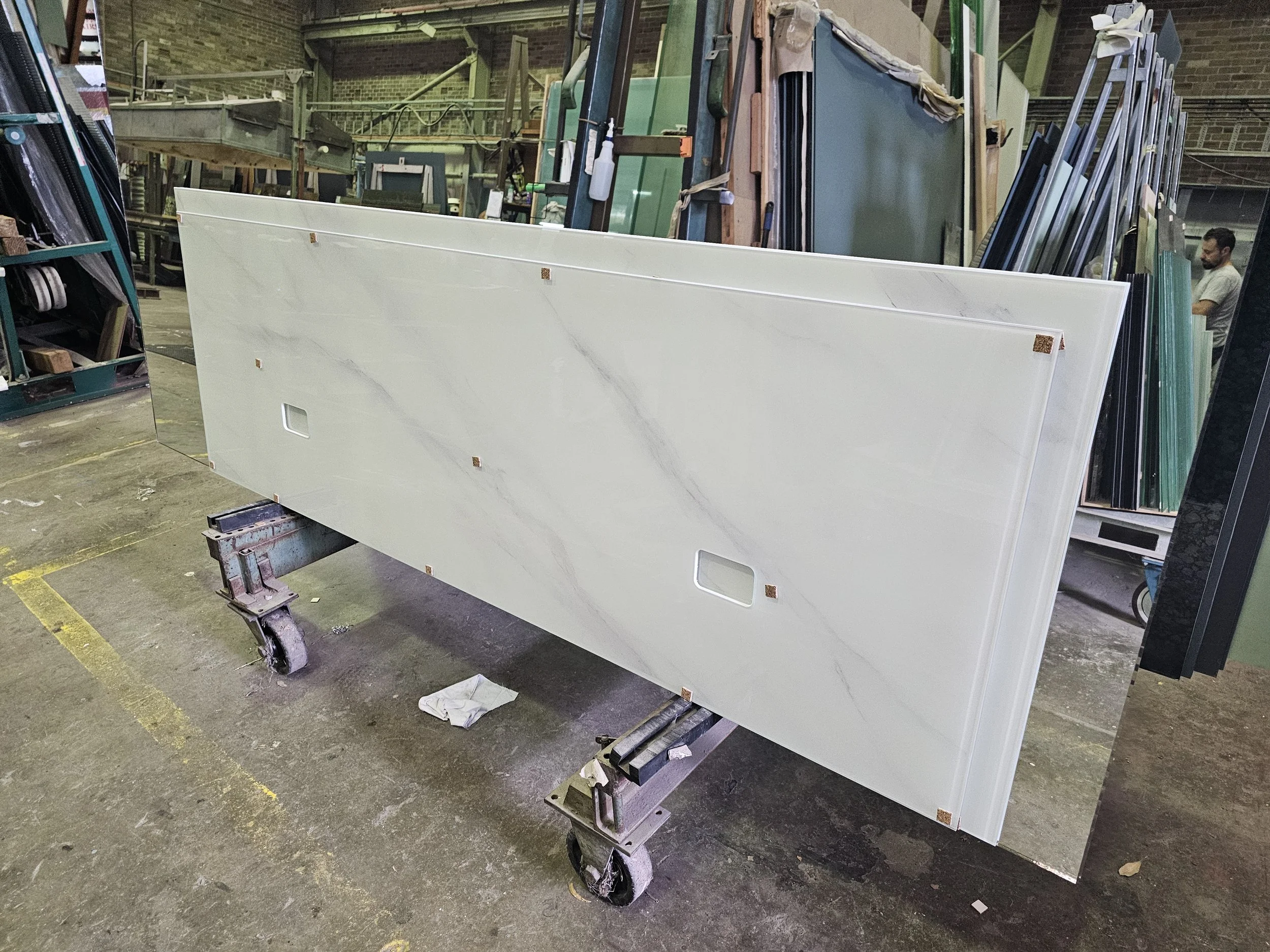 A large marble or quartz slab with white and gray veining, standing upright on a wheeled cart in a factory or warehouse with other similar slabs behind it.