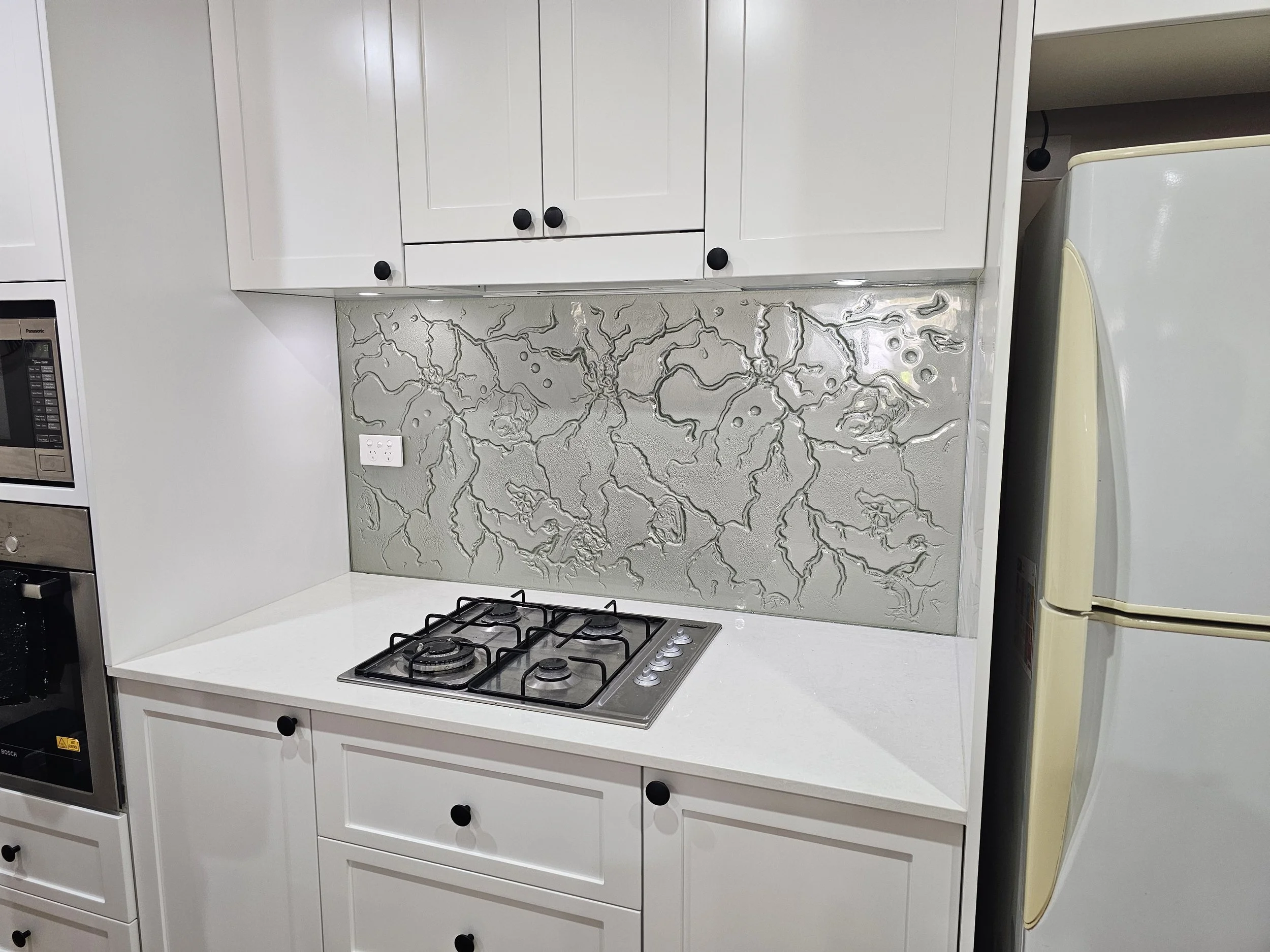 White kitchen with a gas stove, a decorative backsplash, white cabinets with black knobs, and a partially visible refrigerator on the right.