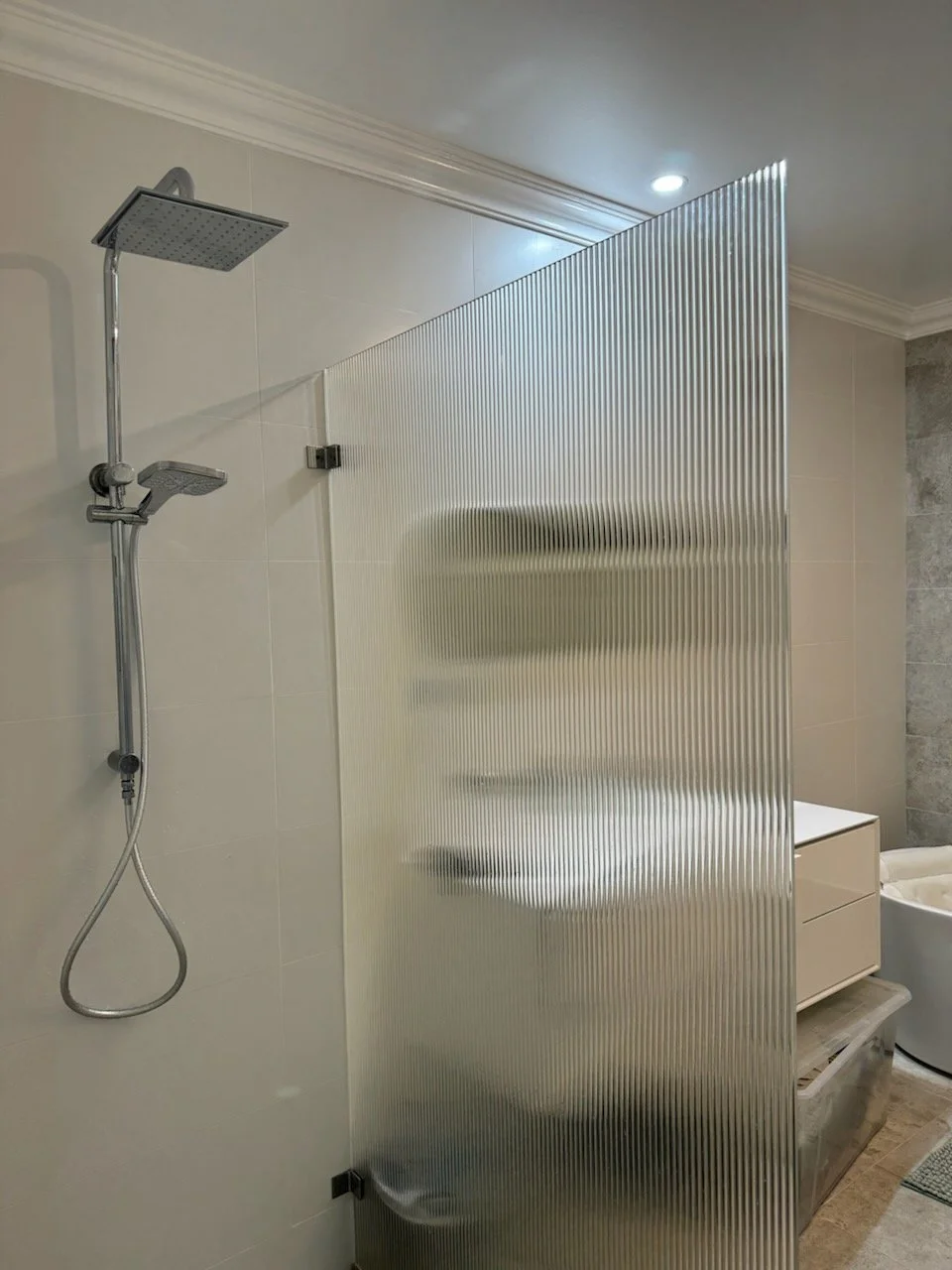 Bathroom with semi-transparent corrugated partition, shower area with rain showerhead, and a modern bathtub.