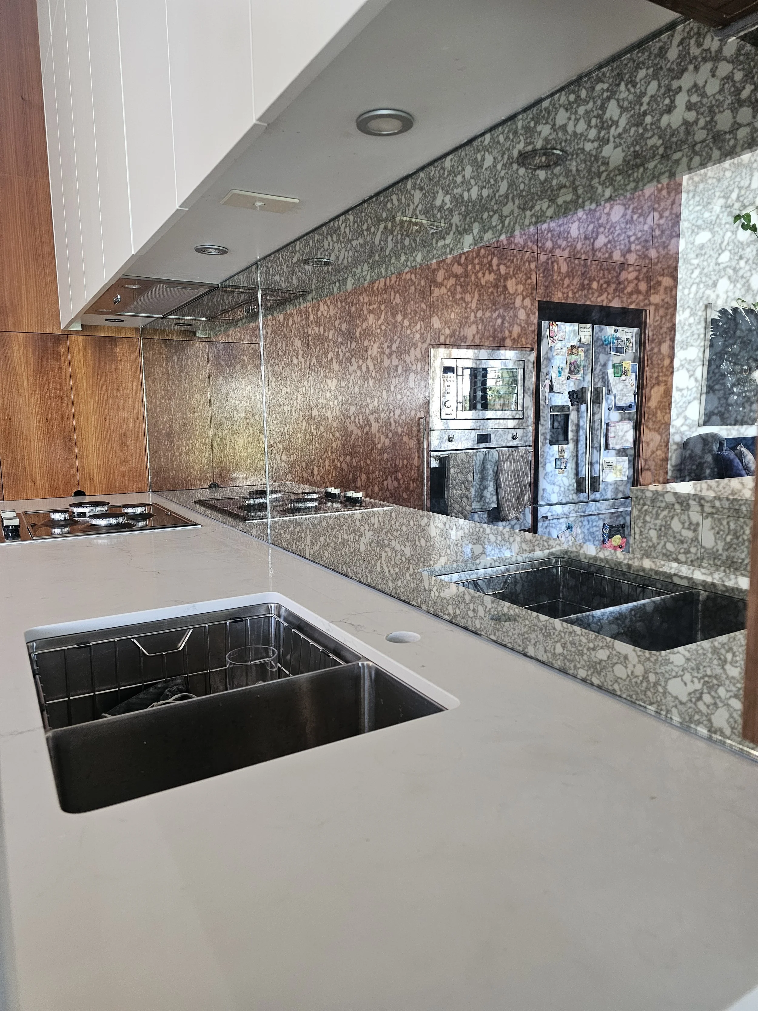 Kitchen with granite countertop, double sink, and mirror reflecting appliances and refrigerator.