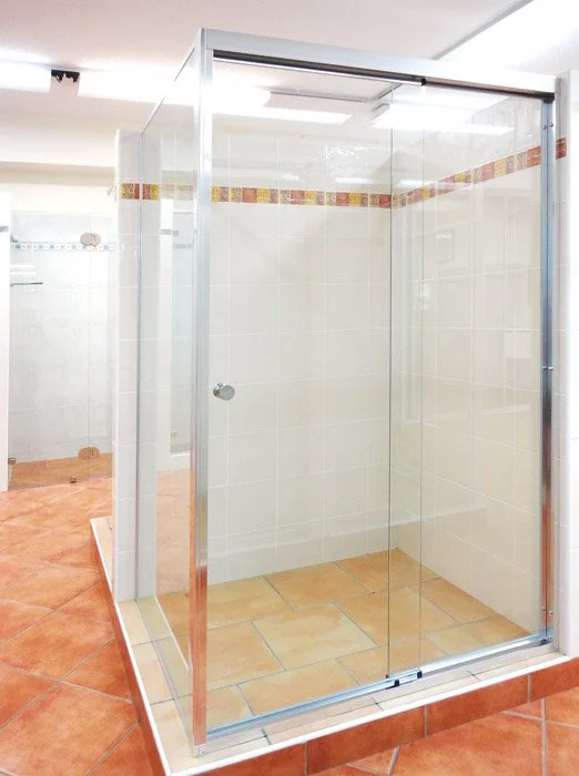 A bathroom under construction with a marble tiled wall, a black-framed mirror, a small white vanity with boxes on top, a black faucet, and a corrugated metal door.