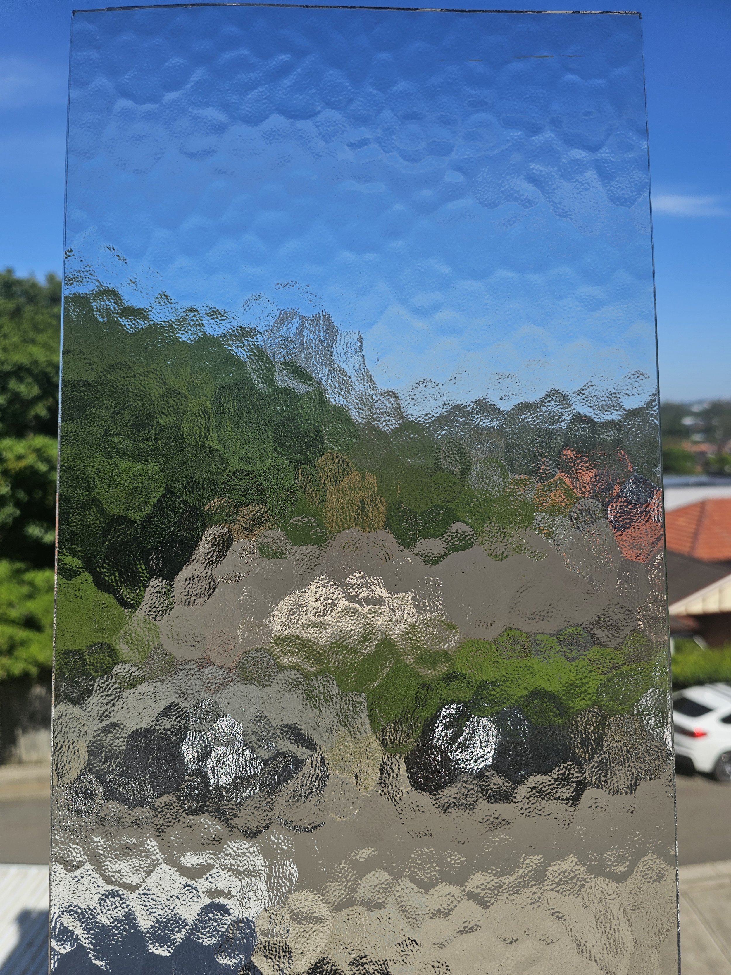 A textured glass or plastic panel distorts the view of a garden and sky behind it, creating an abstract, rippled effect.