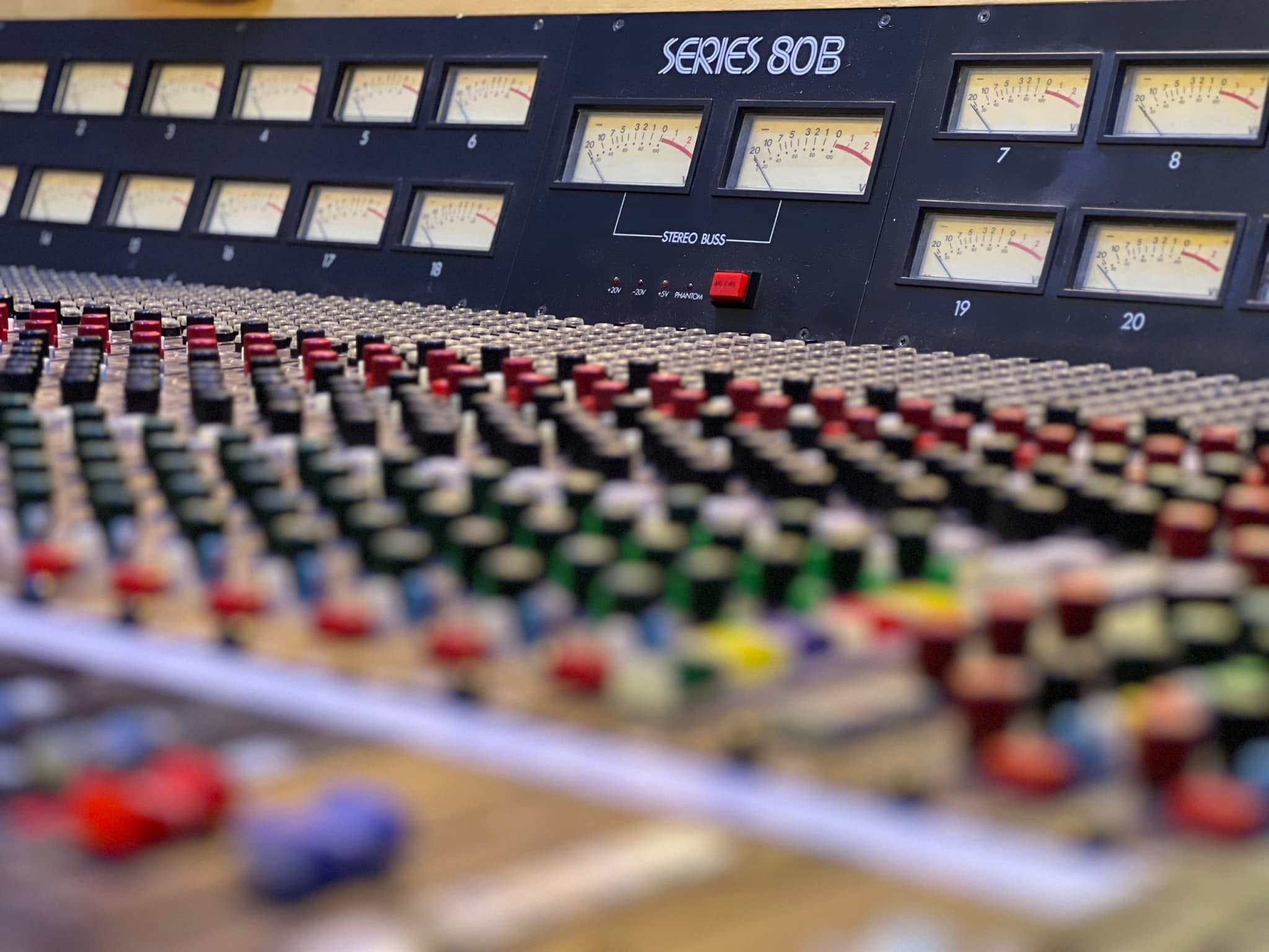Close-up of a professional audio mixing console with numerous colorful knobs and meters.