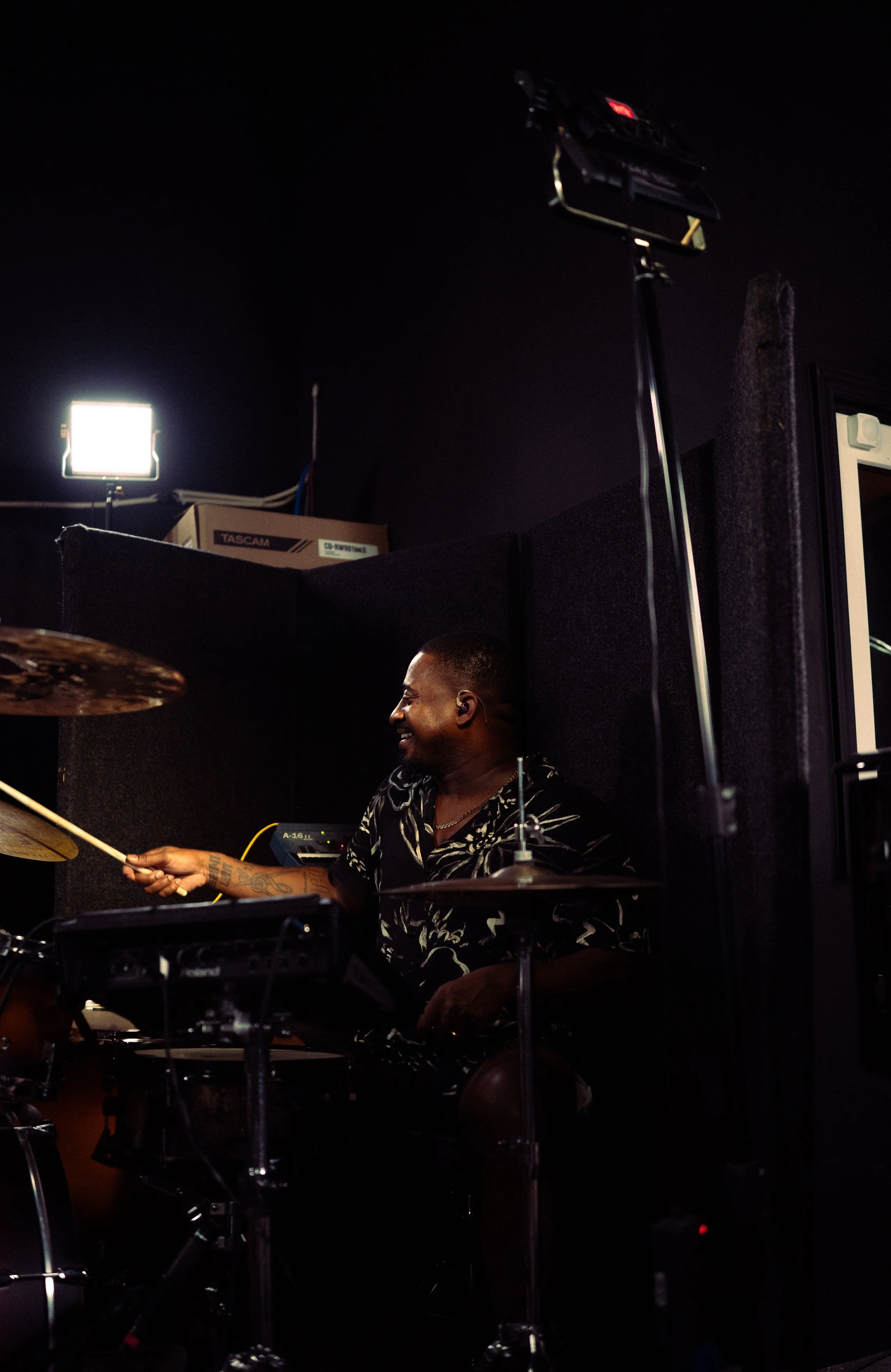 A man playing drums in a recording studio with professional lighting equipment.
