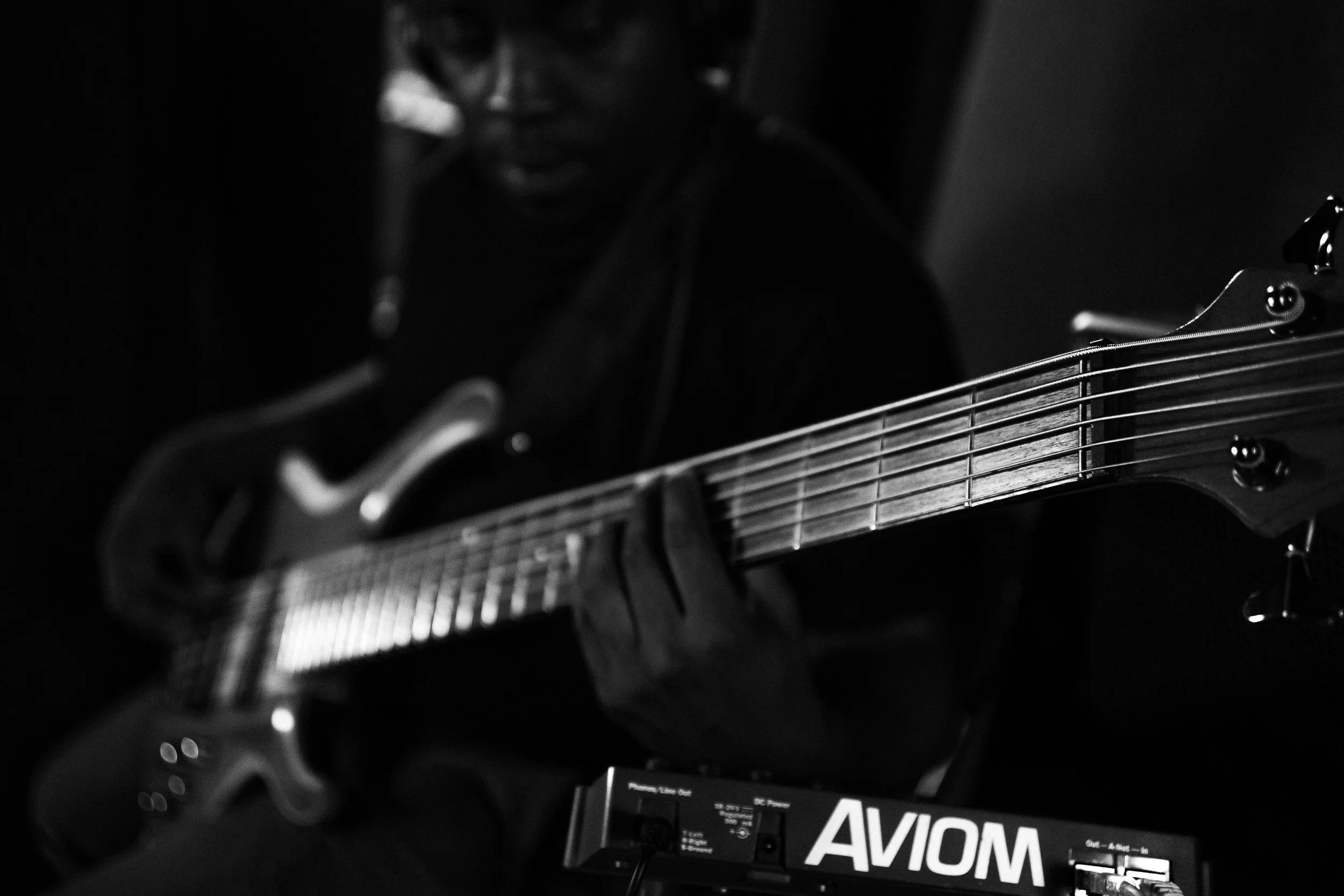 A person playing an electric guitar, shrouded in dark lighting, with a focused expression, and equipment labeled 'AViOM' nearby.
