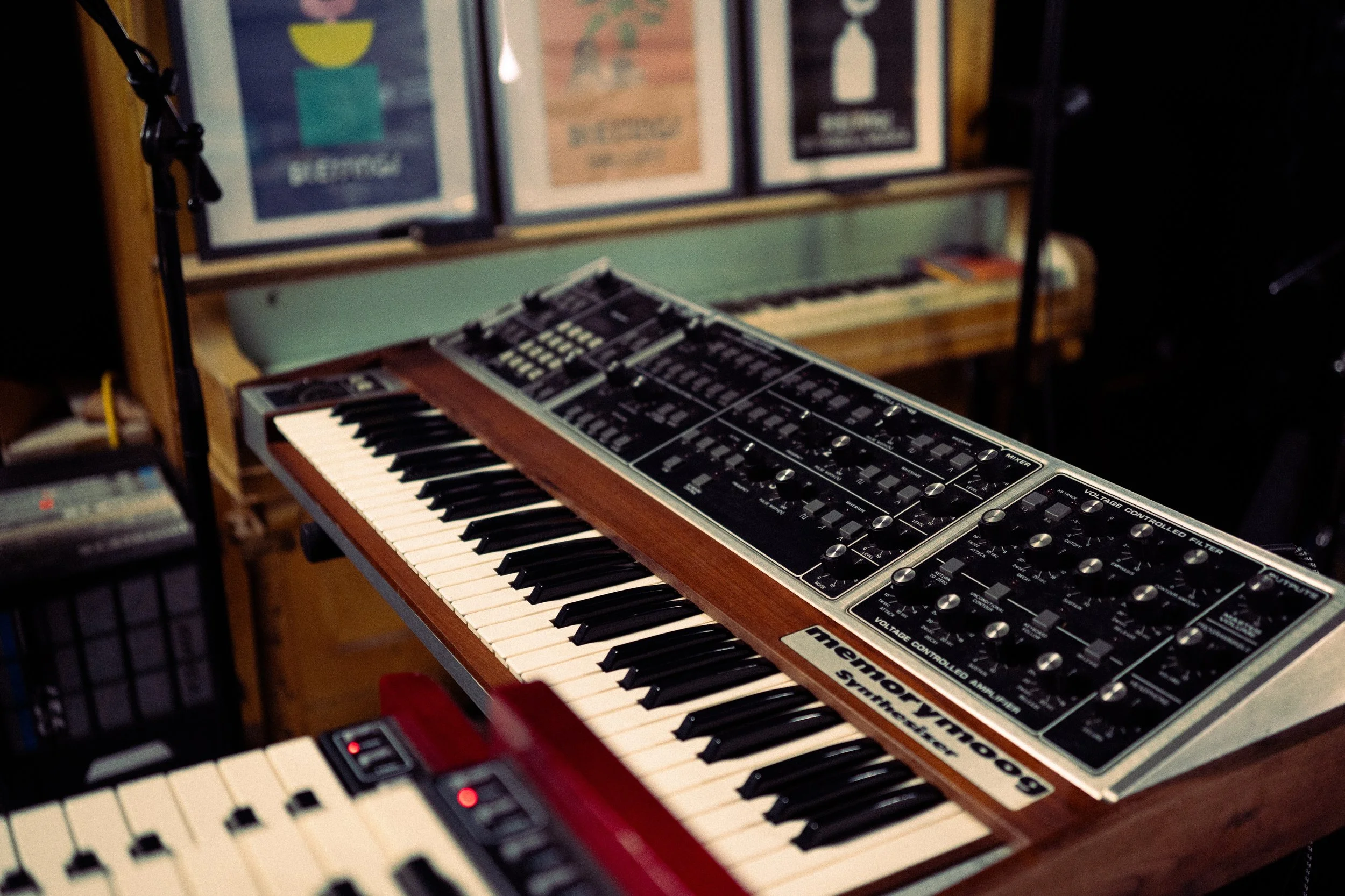 Vintage music keyboard synthesizer with control knobs and switches, placed on a wooden stand in a music studio.