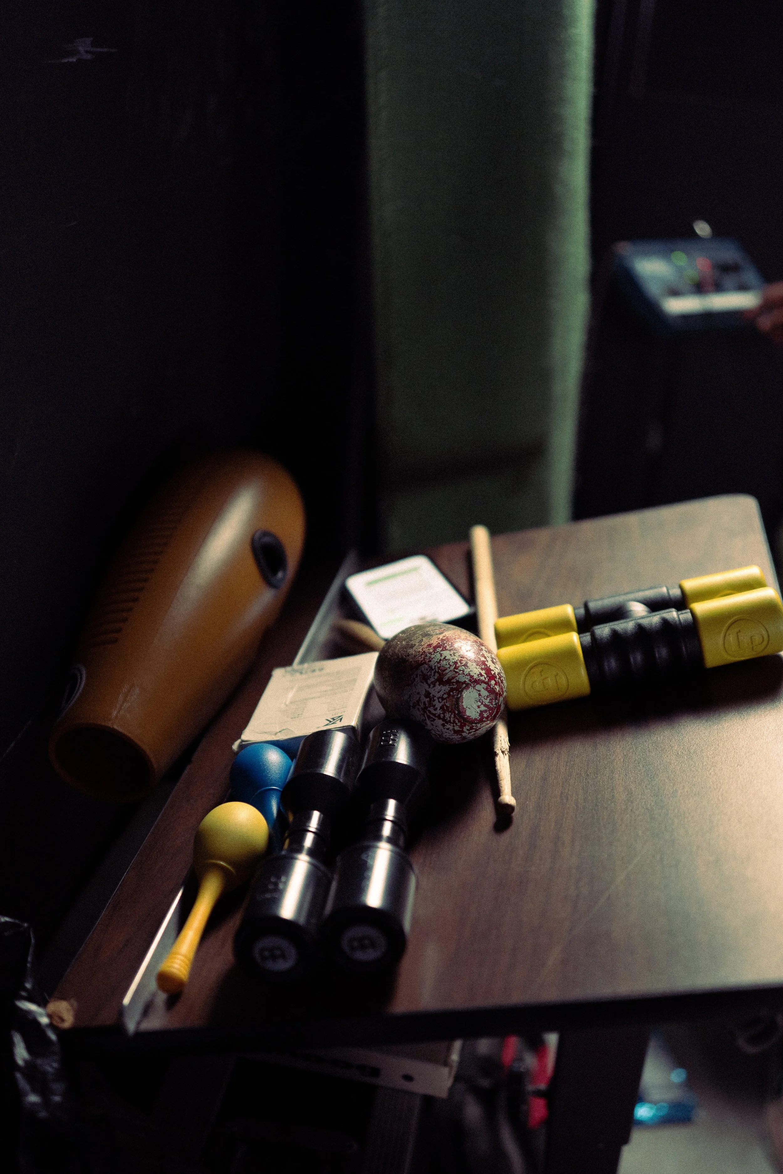 A table with various fitness equipment, including dumbbells, a kettlebell, a foam roller, a massage stick, and a water bottle, in a dimly lit room.