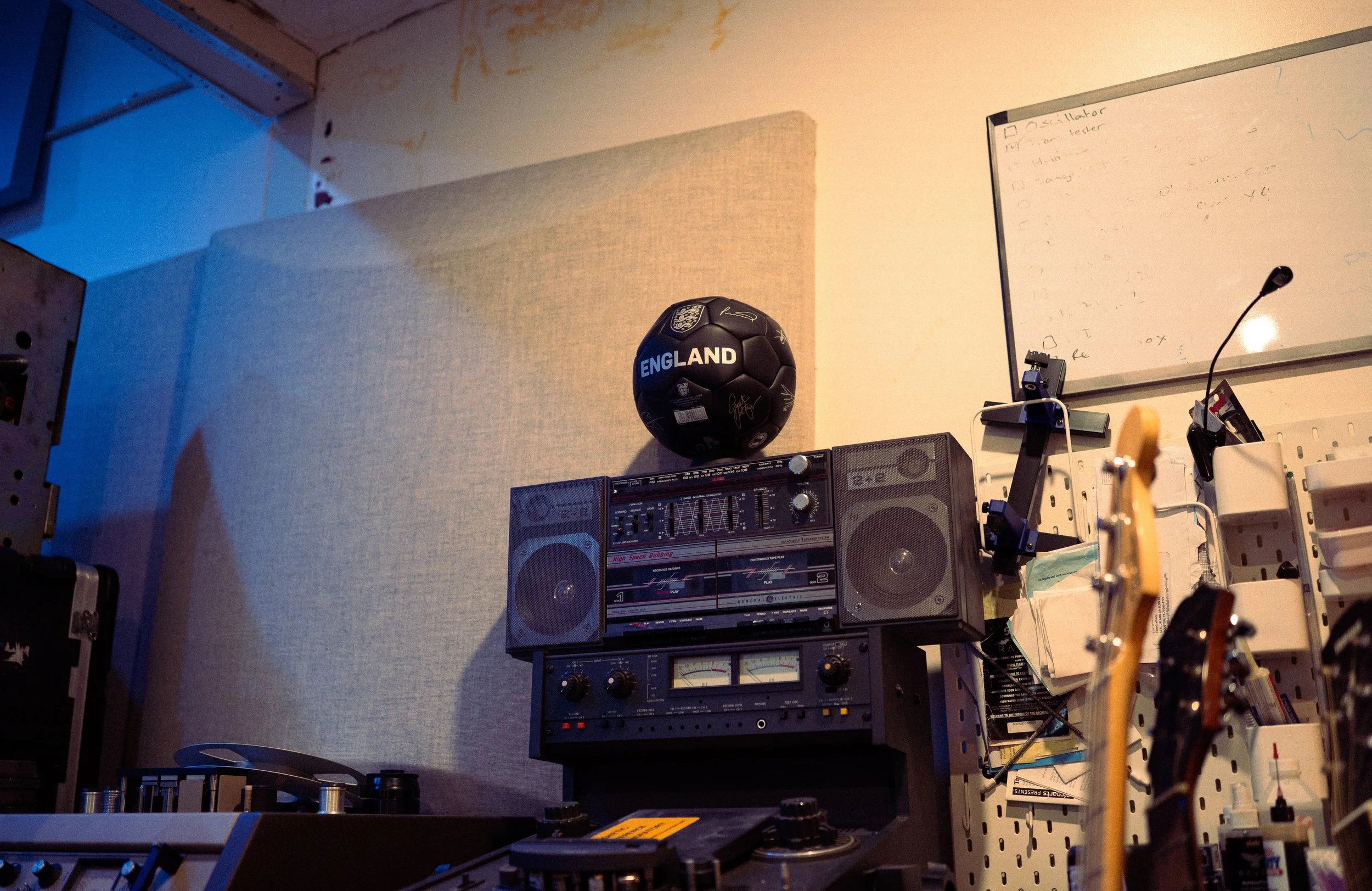A room decorated for a sports fan with a black soccer ball on top of a vintage stereo system, a whiteboard with writing, and musical instruments in the foreground.