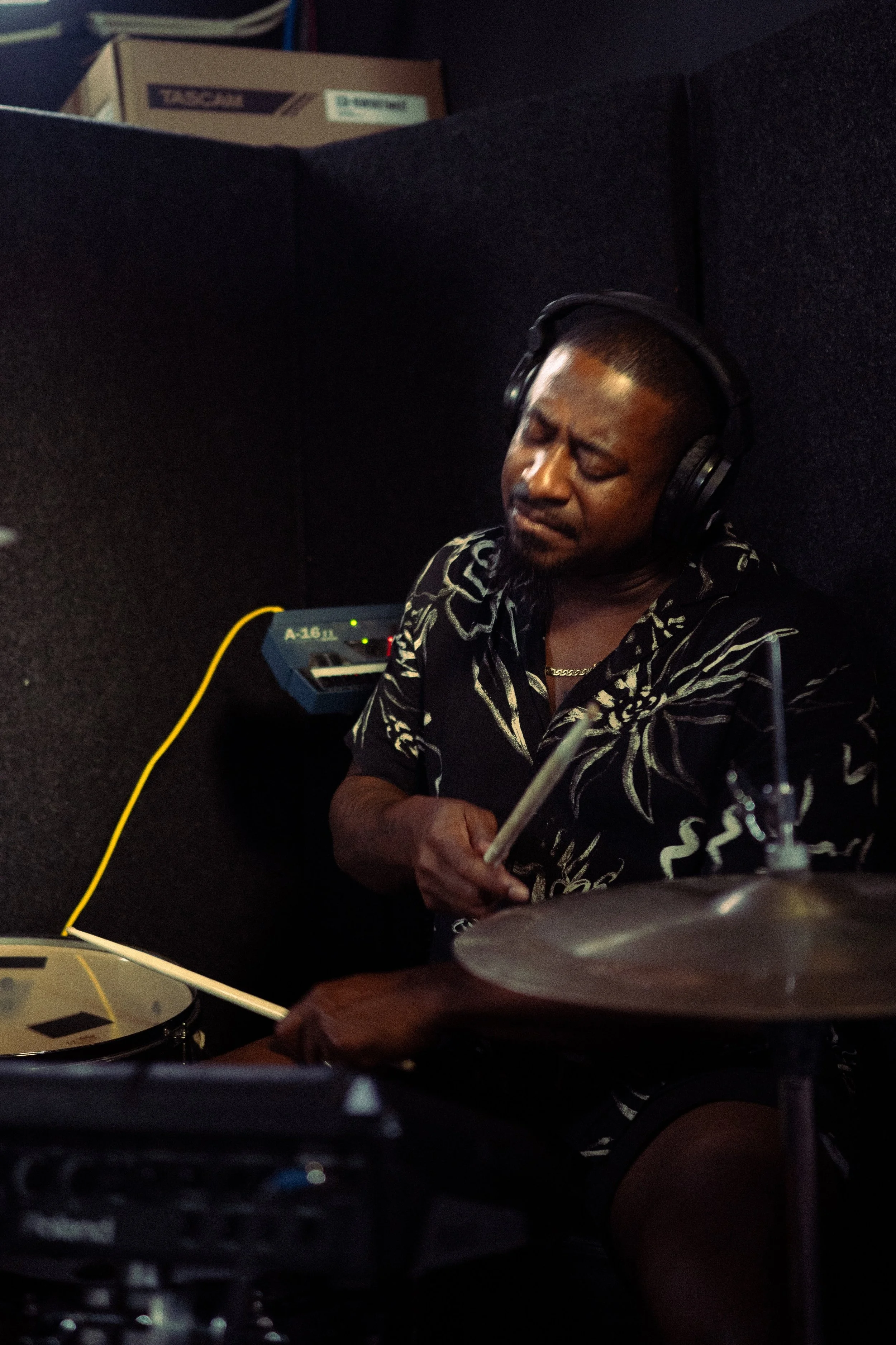 A man wearing headphones playing drums in a soundproof music studio.