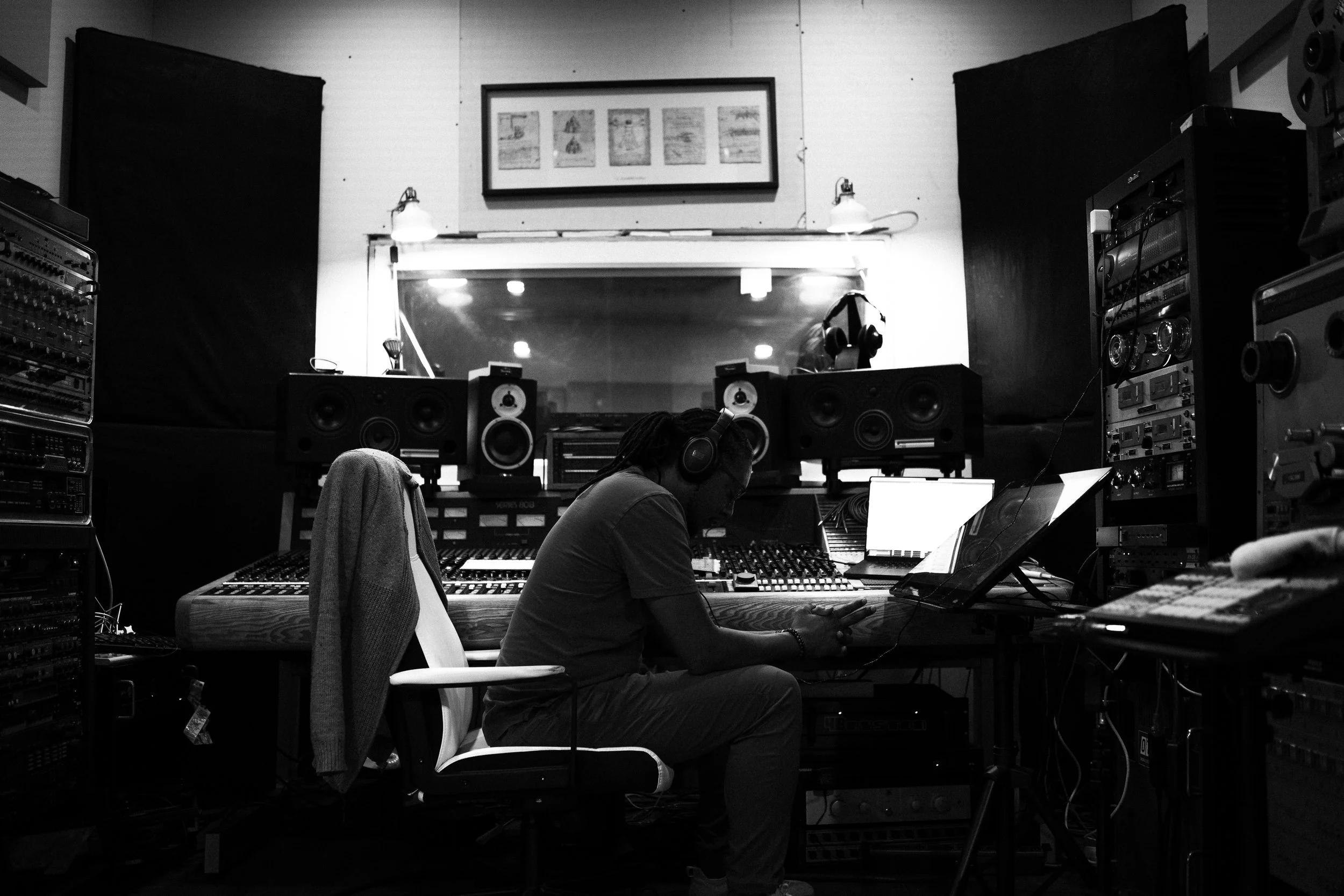 A man working in a professional music recording studio with headphones, surrounded by audio equipment and speakers.